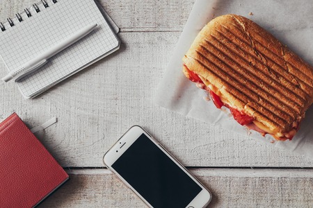 Panini with cellphone, pen and notepad on office wooden tableの写真素材