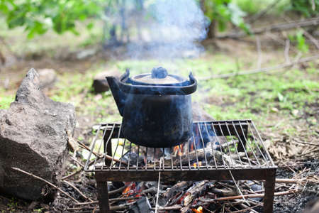 black old smoked teapot on the campfire on picnic in wood in the summer 
