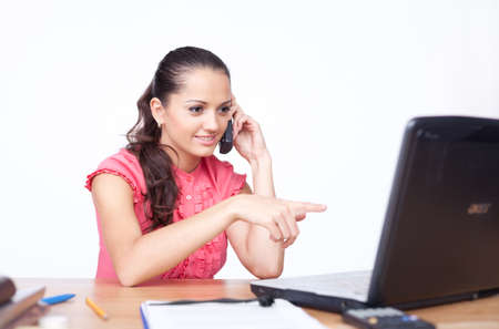 beautiful young woman sitting at office desk and talking on cell phone の写真素材