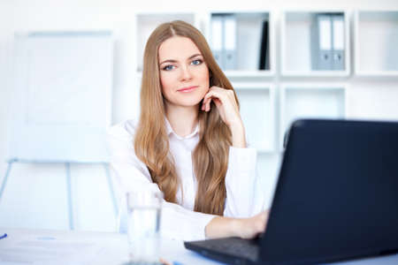 Portrait of beautiful young smiling business woman working on a laptop at officeの写真素材