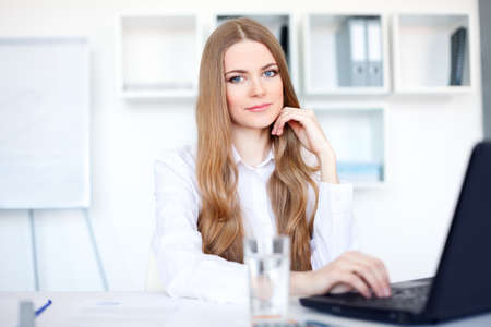 Portrait of beautiful young smiling business woman working on a laptop at officeの写真素材