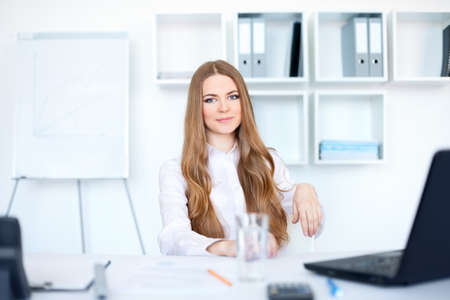 Portrait of beautiful young smiling business woman sitting at  desk in officeの写真素材