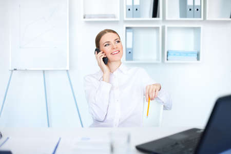 beautiful young business woman sitting at office desk and talking on cell phone の写真素材