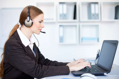 Portrait of pretty young female operator sitting at office desk with headsetの写真素材