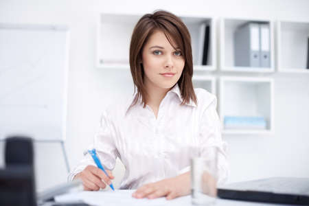 Portrait of a beautiful young smiling business woman doing some paperwork in bright office の写真素材