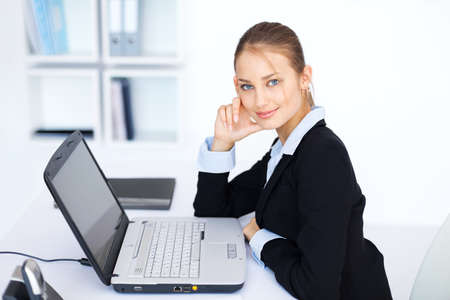Portrait of beautiful young smiling business woman working on a laptop in officeの写真素材