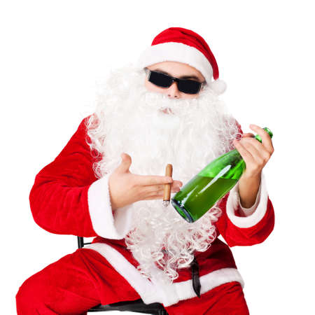 Santa Claus sitting in a chair wearing sunglasses holds a bottle of champagne and smoking a cigar isolated on white backgroundの写真素材
