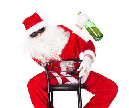 Santa Claus sitting in a chair wearing sunglasses holds a bottle of champagne and smoking a cigar isolated on white backgroundの写真素材