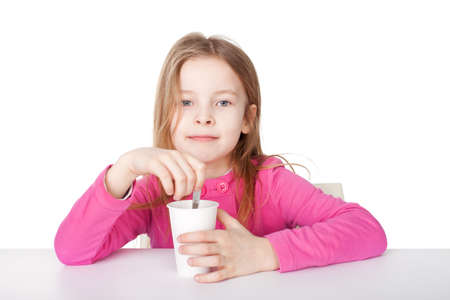 Cute little girl in red shirt drinking tea while sitting at table isolated on white backgroundの写真素材