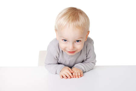 Cute little smiling boy sitting at table isolated on white backgroundの写真素材