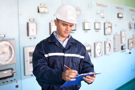 Portrait of young smiling engineer taking notes at control roomの写真素材