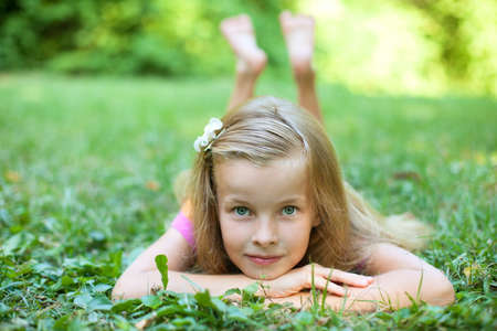Beautiful little girl is lying on the green grassの写真素材