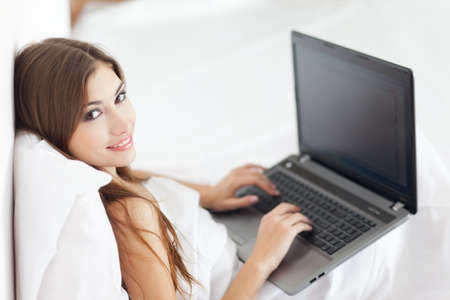 Portrait of beautiful young woman with laptop on bedの写真素材