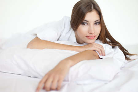 Beautiful happy smiling young woman in large shirt on bedの写真素材