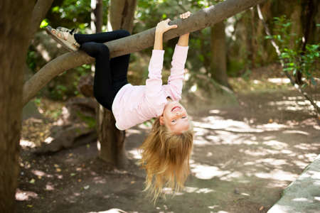 Ð¡ute little girl playfully hangs from a tree limbの写真素材