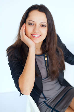 Portrait of young smiling brunette business woman sitting on a chair on white backgroundの写真素材