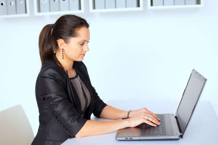 Portrait of beautiful young brunette business woman working on a laptop in office