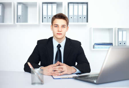 Portrait of young serious businessman at his workplace in bright officeの写真素材