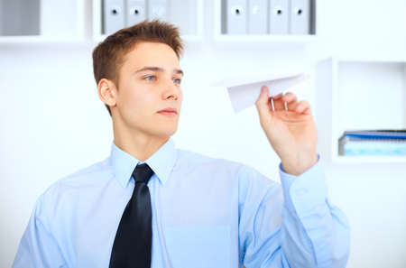 Portrait of young businessman launch a paper airplane at his workplace in bright officeの写真素材