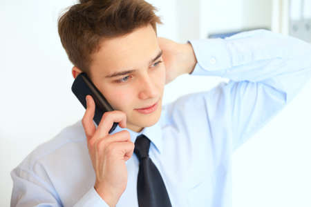 Portrait of young smiling businessman talking on cell phone in officeの写真素材