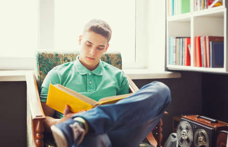 Student at home sitting on chair and reading bookの写真素材