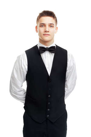 Portrait of young smiling waiter standing with hands behind his back isolated on white backgroundの写真素材