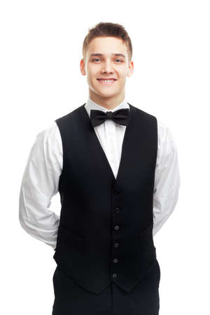 Portrait of young smiling waiter standing with hands behind his back isolated on white backgroundの写真素材