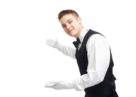 Portrait of young happy smiling waiter gesturing welcome isolated on white backgroundの写真素材