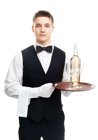 Portrait of young happy smiling waiter with bottle of white wine and stemware glass on tray isolated on white backgroundの写真素材