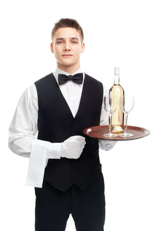 Portrait of young happy smiling waiter with bottle of white wine and stemware glass on tray isolated on white backgroundの写真素材