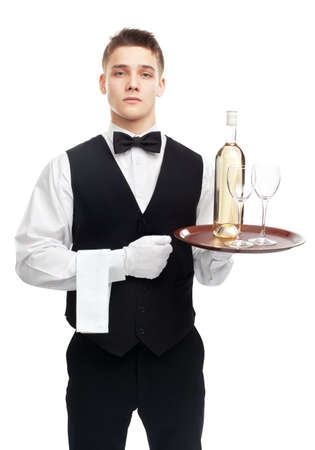 Portrait of young serious waiter with bottle of white wine and stemware glass on tray isolated on white backgroundの写真素材