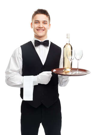 Portrait of young happy smiling waiter with bottle of white wine and stemware glass on tray isolated on white backgroundの写真素材