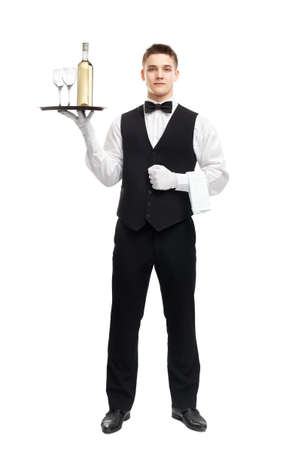 full length portrait of young happy smiling waiter with bottle of white wine and stemware glass on tray isolated on white backgroundの写真素材