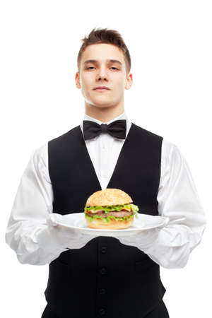 Portrait of young serious waiter holding burger on plate isolated on white backgroundの写真素材