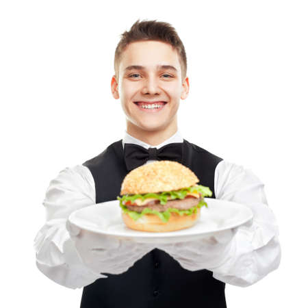 Portrait of young happy smiling waiter holding hamburger on plate isolated on white backgroundの写真素材