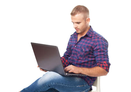 Young man sitting in chair and working on laptop computer isolated on white backgroundの写真素材