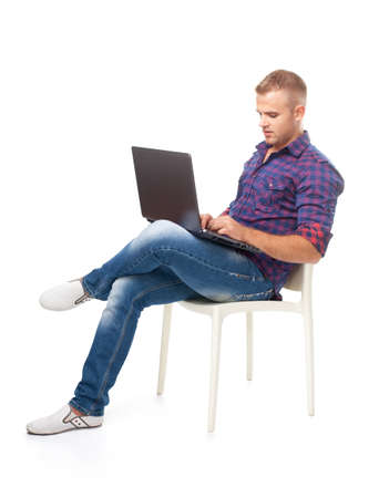 Young man sitting in chair and working on laptop computer isolated on white backgroundの写真素材