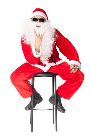 Santa Claus wearing sunglasses sitting in a chair showing the rocker hand sign and smoking a cigar isolated on white backgroundの写真素材