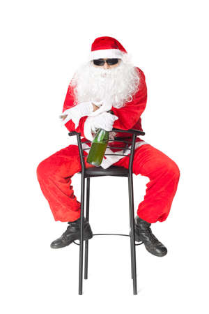 Santa Claus sitting in a chair wearing sunglasses holds a bottle of champagne and smoking a cigar isolated on white background の写真素材