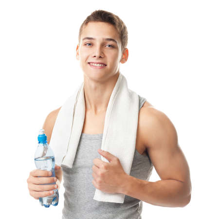 Portrait of young smiling athlete man with a white towel on his shoulder holding a water bottle isolated on white の写真素材