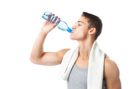 Young muscular athlete man with a white towel on his shoulder drinking water isolated on white の写真素材