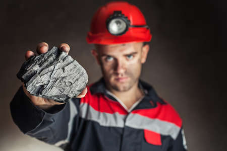Coal miner showing lump of coal against a dark backgroundの写真素材