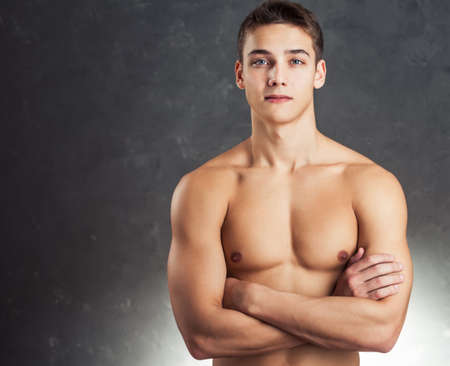 Portrait of smiling muscular young man with naked torso against gray textured backgroundの写真素材