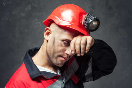 Portrait of tired coal miner wiping forehead his hand against a dark background