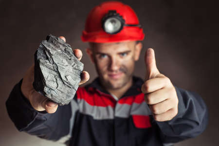 Coal miner showing lump of coal with thumbs up against a dark background