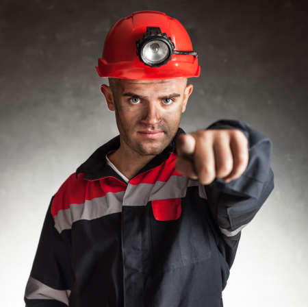 Portrait of serious coal miner pointing forward against a dark backgroundの写真素材