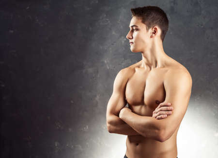 Portrait of muscular young man looking away with naked torso against gray textured backgroundの写真素材