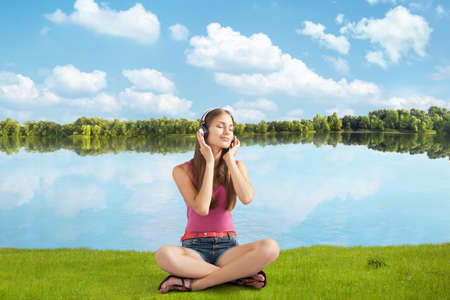 beautiful girl in headphones listens to music near river, sitting ashore の写真素材