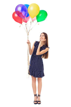 Full length portrait of beautiful young surprised woman in polka dot dress holding colorful balloons isolated on white backgroundの写真素材