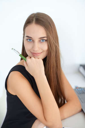Portrait of beautiful young smiling business woman sitting at her workplace in officeの写真素材